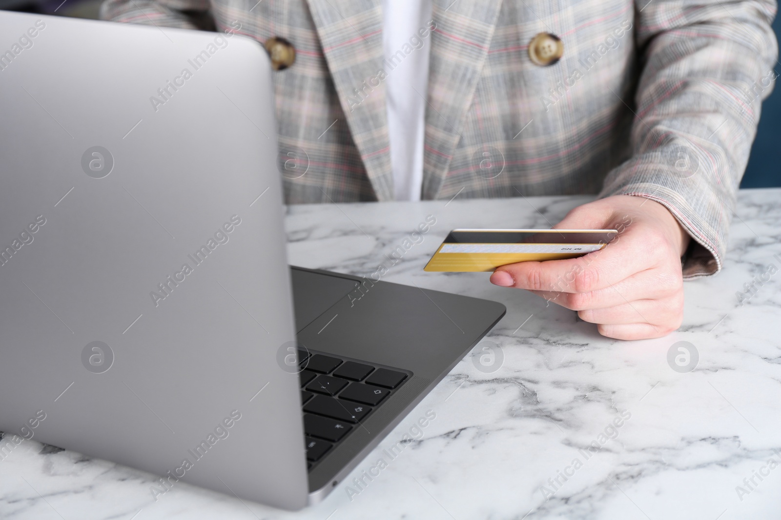 Photo of Online payment. Woman with laptop and credit card at white marble table, closeup