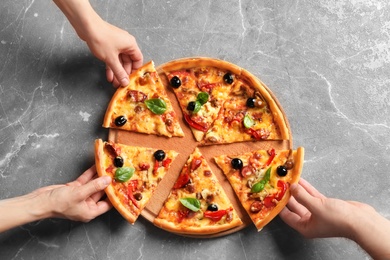 People taking slices of delicious pizza with olives and sausages at table