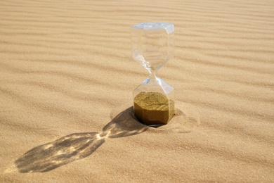 Hourglass with flowing sand in desert on sunny day. Space for text