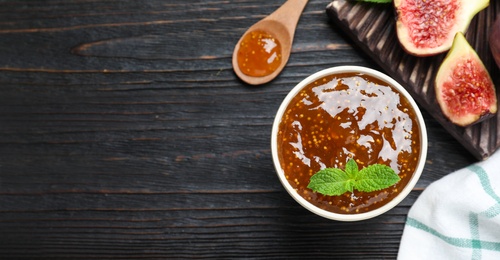 Photo of Flat lay composition with homemade delicious fig jam 
on black wooden table. Space for text