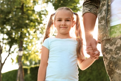 Photo of Father in military uniform walking with his daughter at sunny park