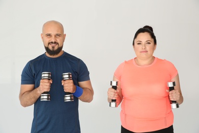 Photo of Overweight man and woman doing exercise with dumbbells on light background