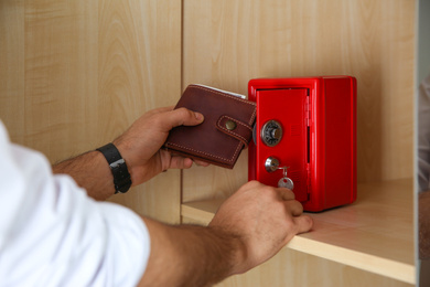 Photo of Man putting wallet into small red steel safe, closeup
