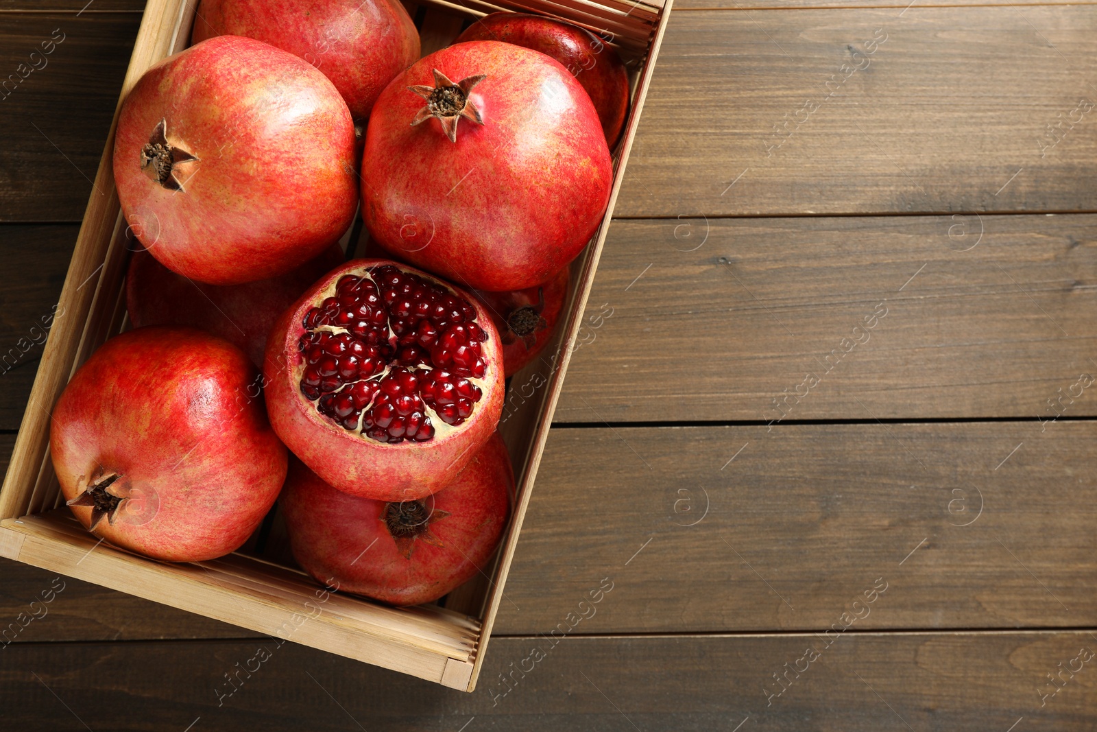 Photo of Ripe pomegranates in crate on wooden table, top view. Space for text