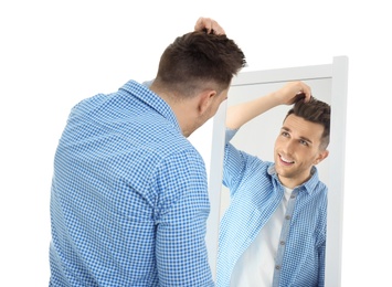 Young man looking at himself in mirror on white background