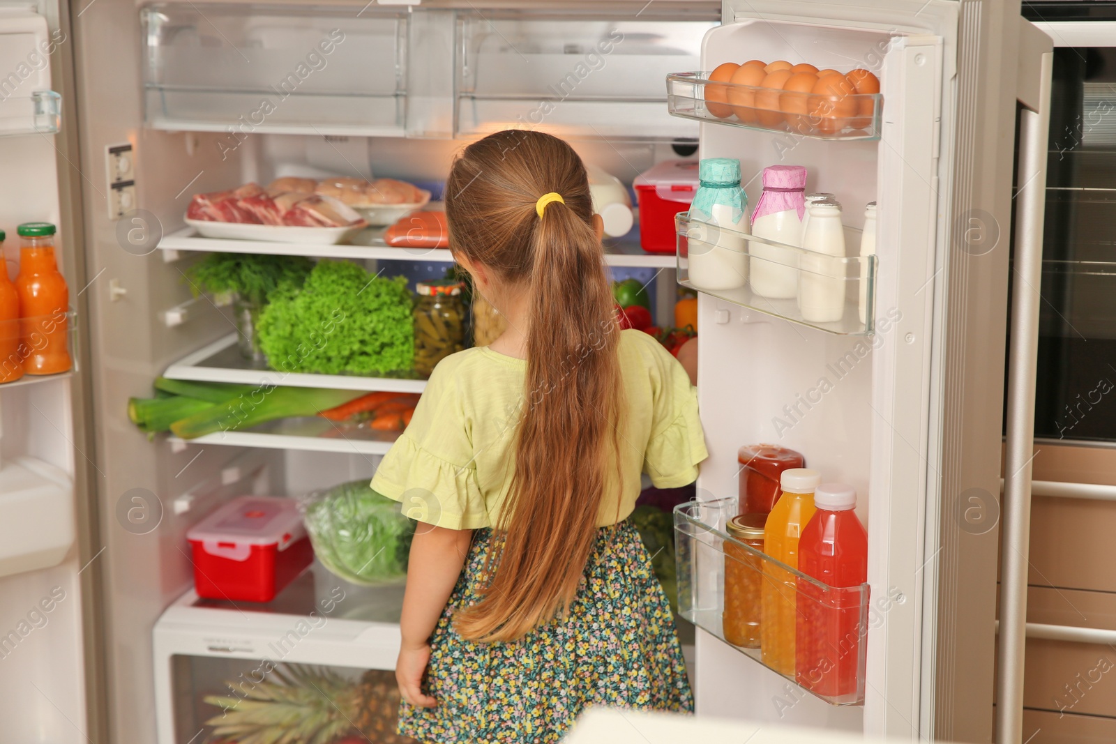 Photo of Cute little girl choosing food in refrigerator at home