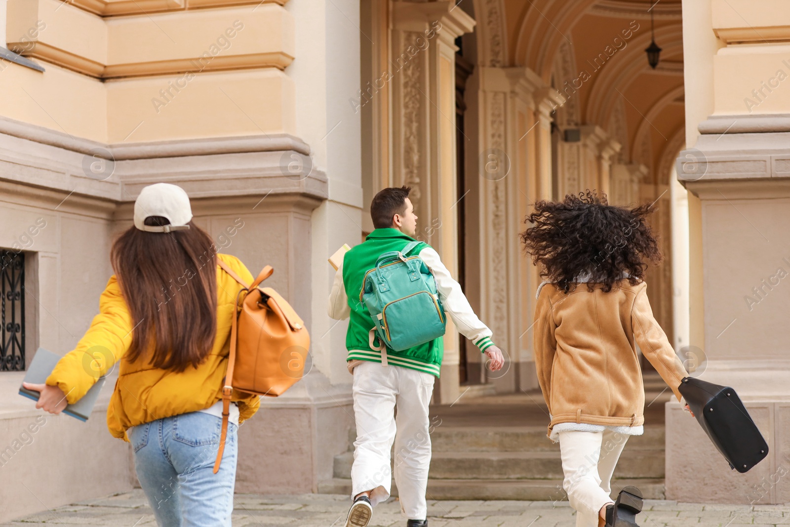 Photo of Being late. Group of students running towards building outdoors, back view