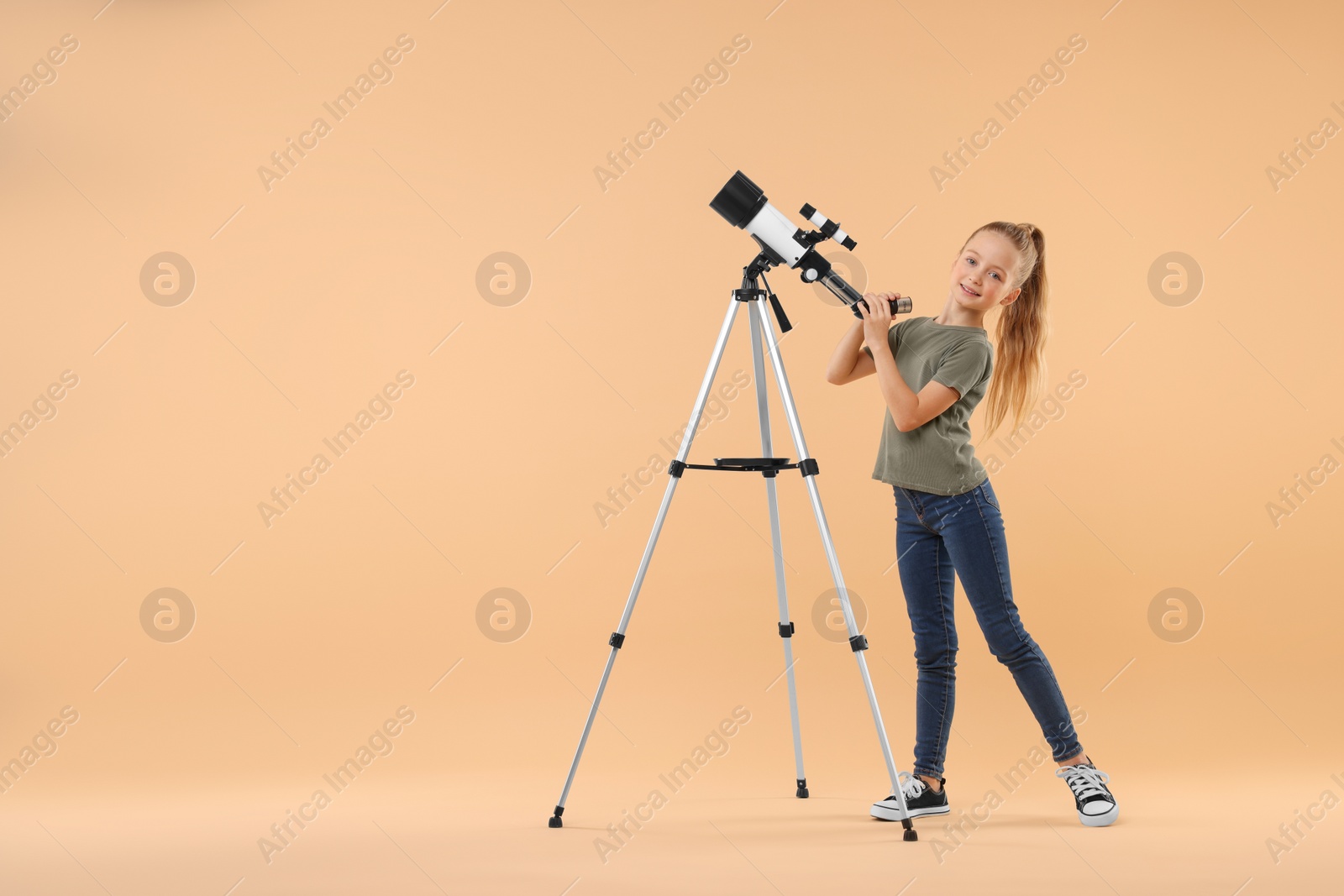 Photo of Happy little girl with telescope on beige background. Space for text