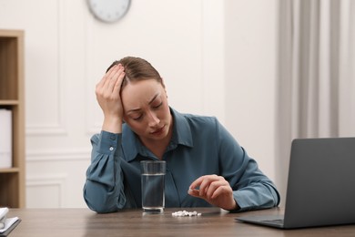 Photo of Depressed woman with antidepressant pills and glass of water at wooden table indoors