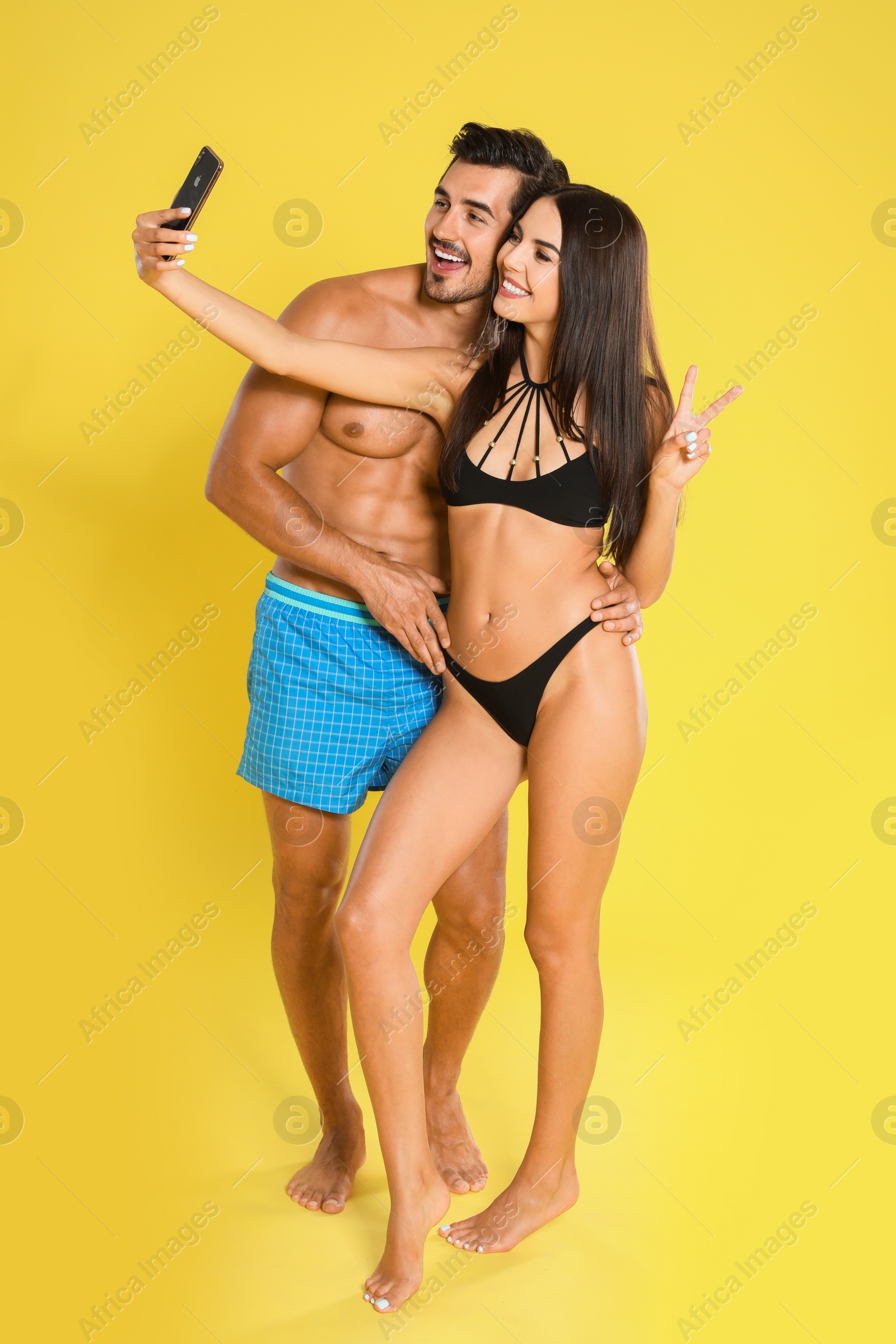 Photo of Young attractive couple in beachwear taking selfie on yellow background