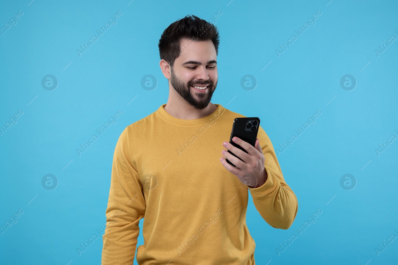 Photo of Happy young man using smartphone on light blue background