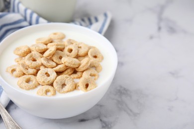 Photo of Breakfast cereal. Tasty corn rings with milk in bowl on white marble table, closeup. Space for text