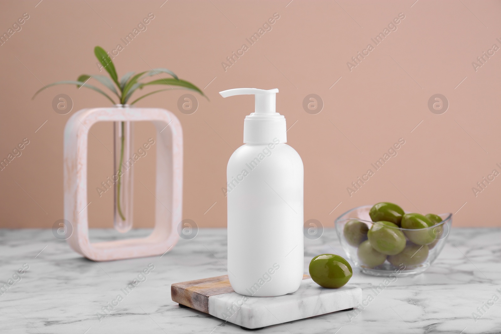 Photo of Bottle of cosmetic product with olive essential oil on white marble table