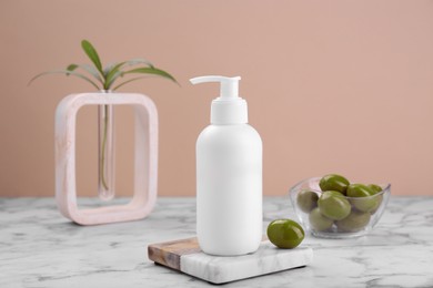 Bottle of cosmetic product with olive essential oil on white marble table