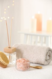 Photo of Spa composition. Sea salt, brush, towel and reed air freshener on soft white surface
