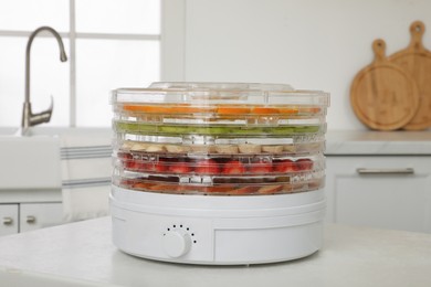 Photo of Dehydrator machine with different fruits and berries on white table in kitchen