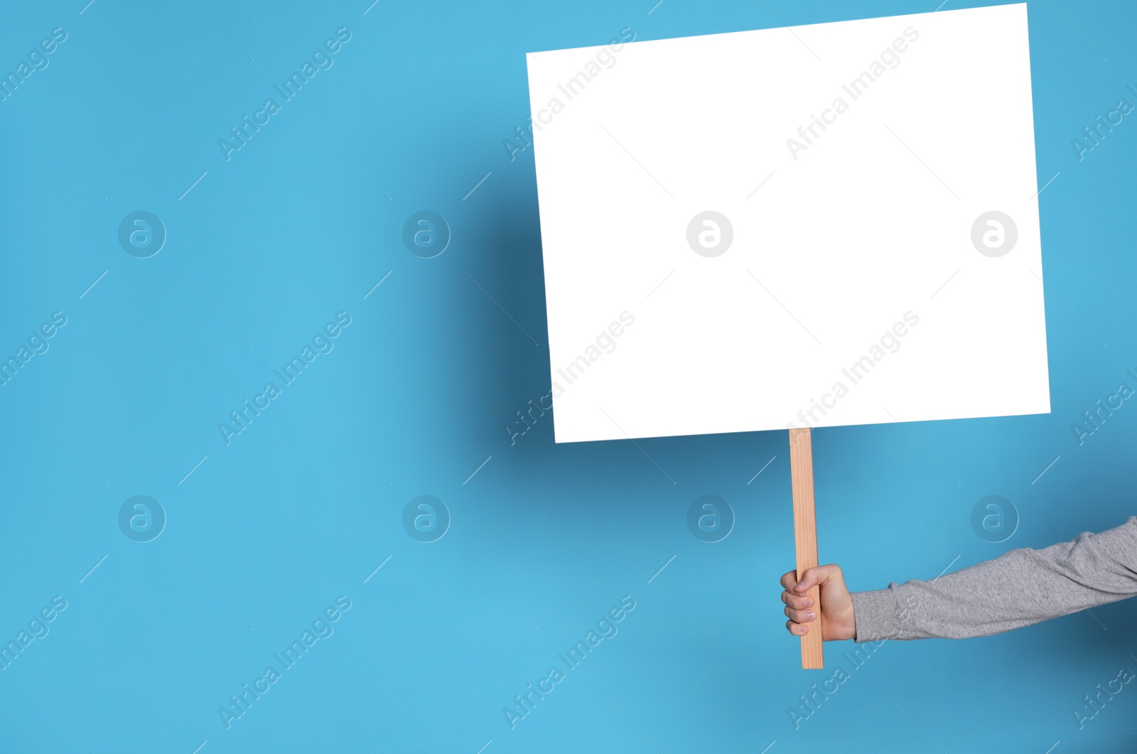 Photo of Woman holding blank sign on light blue background, closeup. Space for text