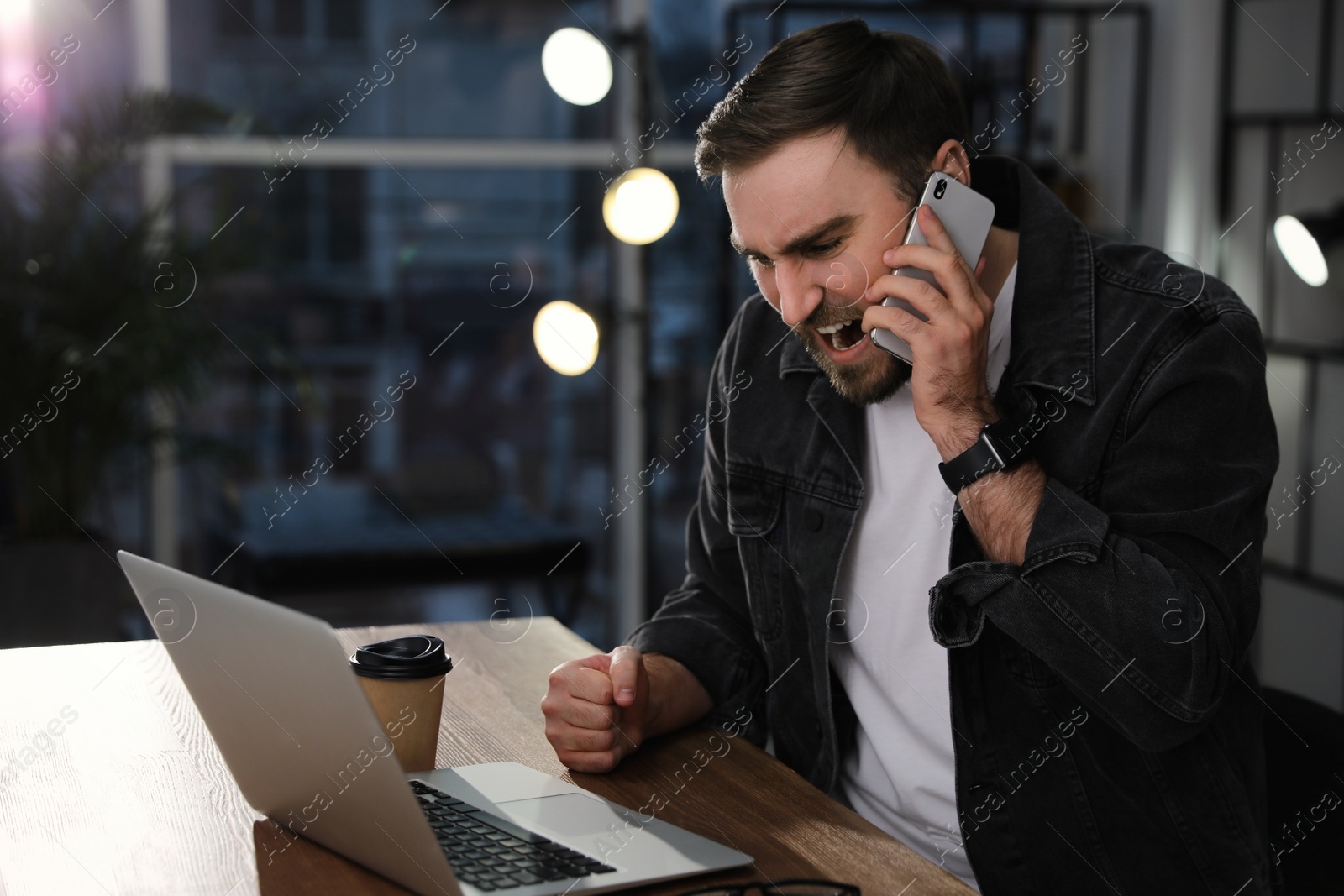 Photo of Emotional man talking on smartphone at workplace in office. Hate concept