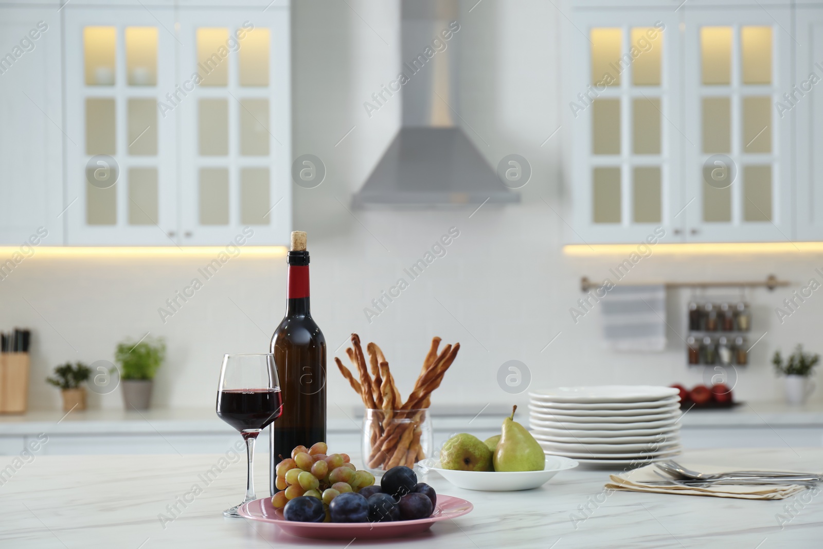 Photo of Red wine and snacks on white table in modern kitchen. Space for text