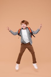 Cute schoolboy with backpack jumping on beige background