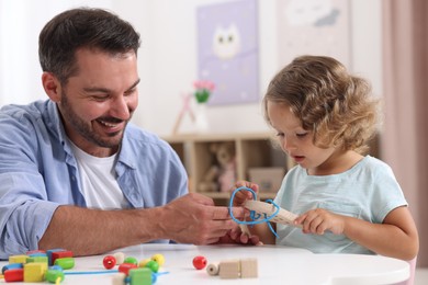 Photo of Motor skills development. Father and daughter playing with wooden lacing toy at table indoors