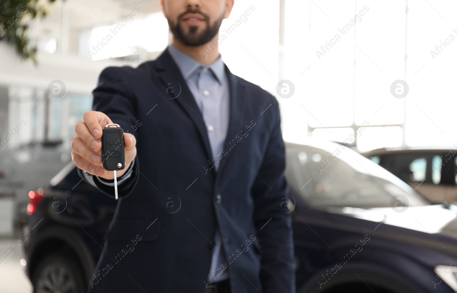 Photo of Salesman with key in modern car salon, closeup