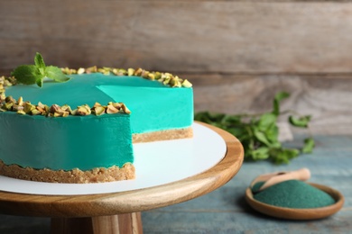 Photo of Dessert stand with tasty spirulina cheesecake on blue wooden table, space for text