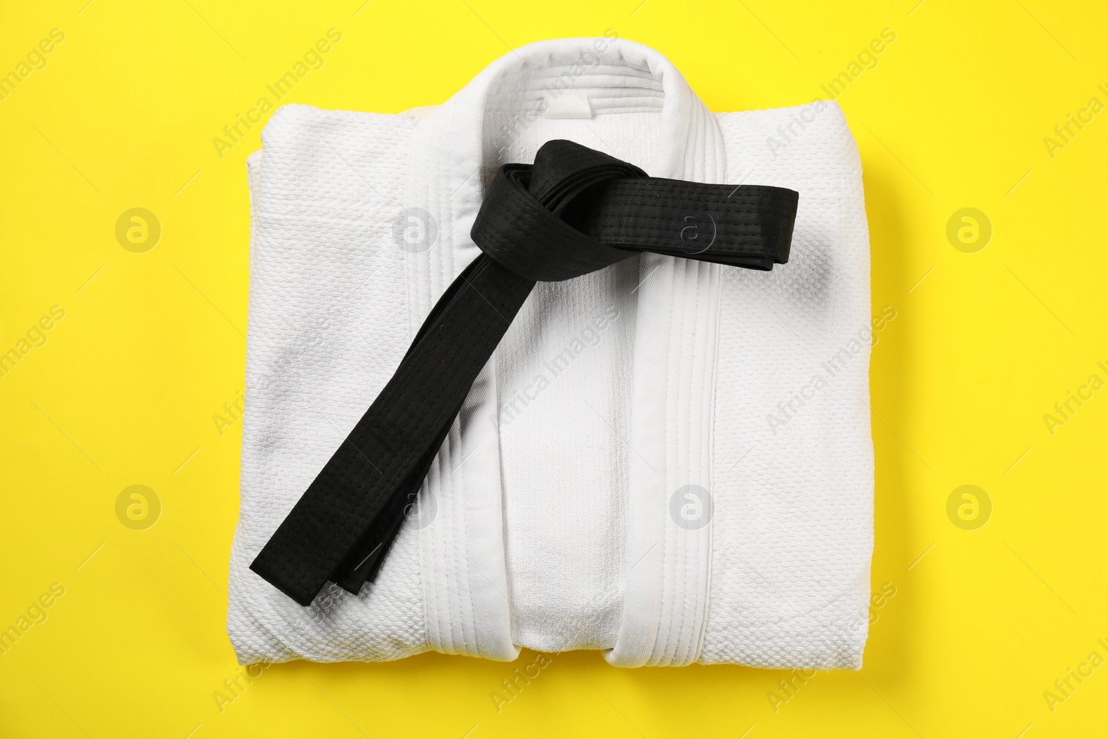 Photo of Black karate belt and white kimono on yellow background, top view