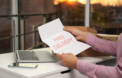 Photo of Woman with note Free Delivery working at table indoors, closeup. Courier service