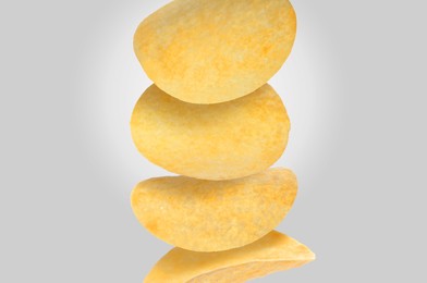 Stack of tasty potato chips on light grey background