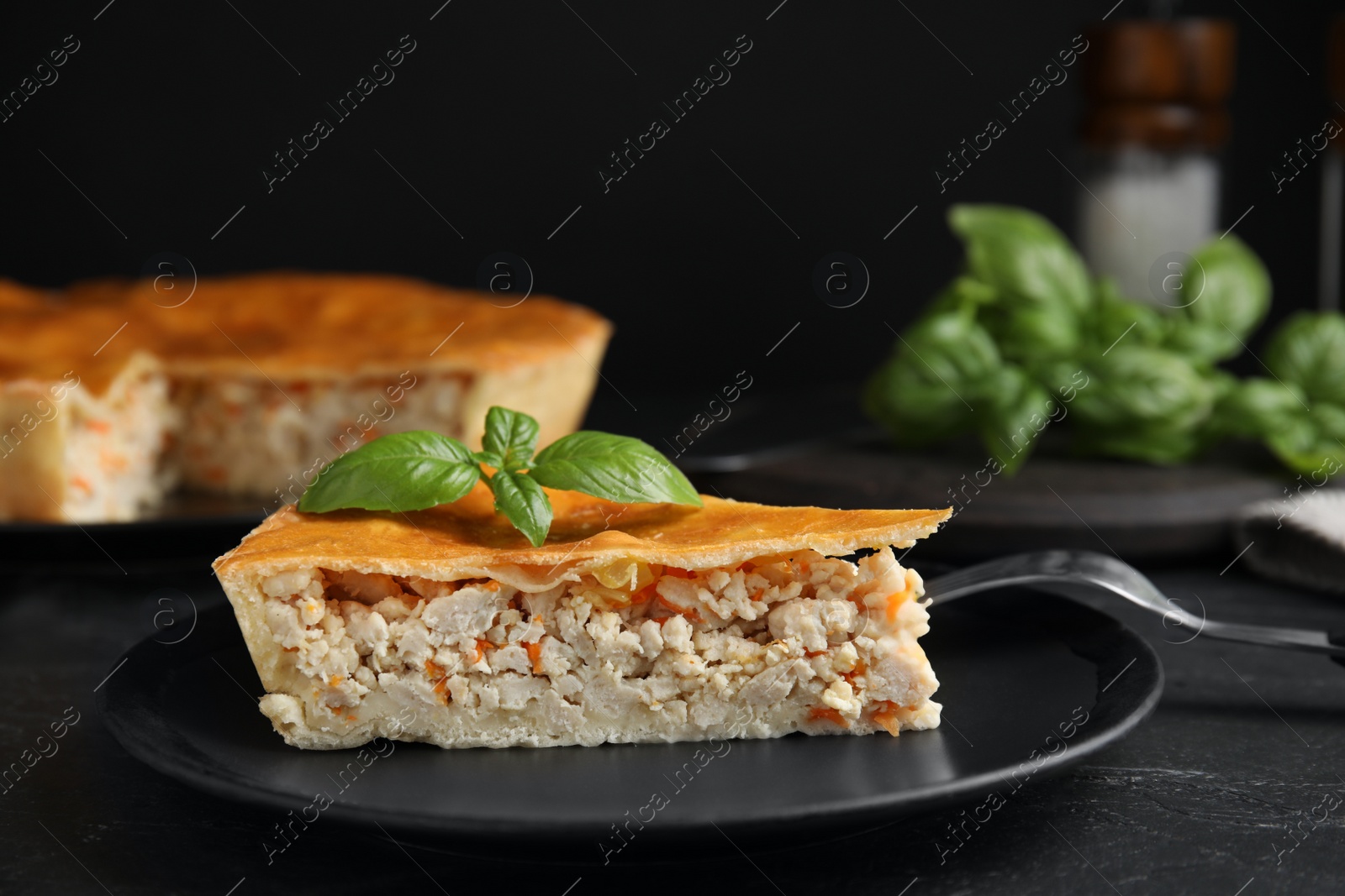 Photo of Piece of delicious pie with meat and basil on black table