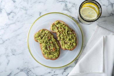 Photo of Delicious sandwiches with guacamole and lemon slices in glass on white marble table, flat lay