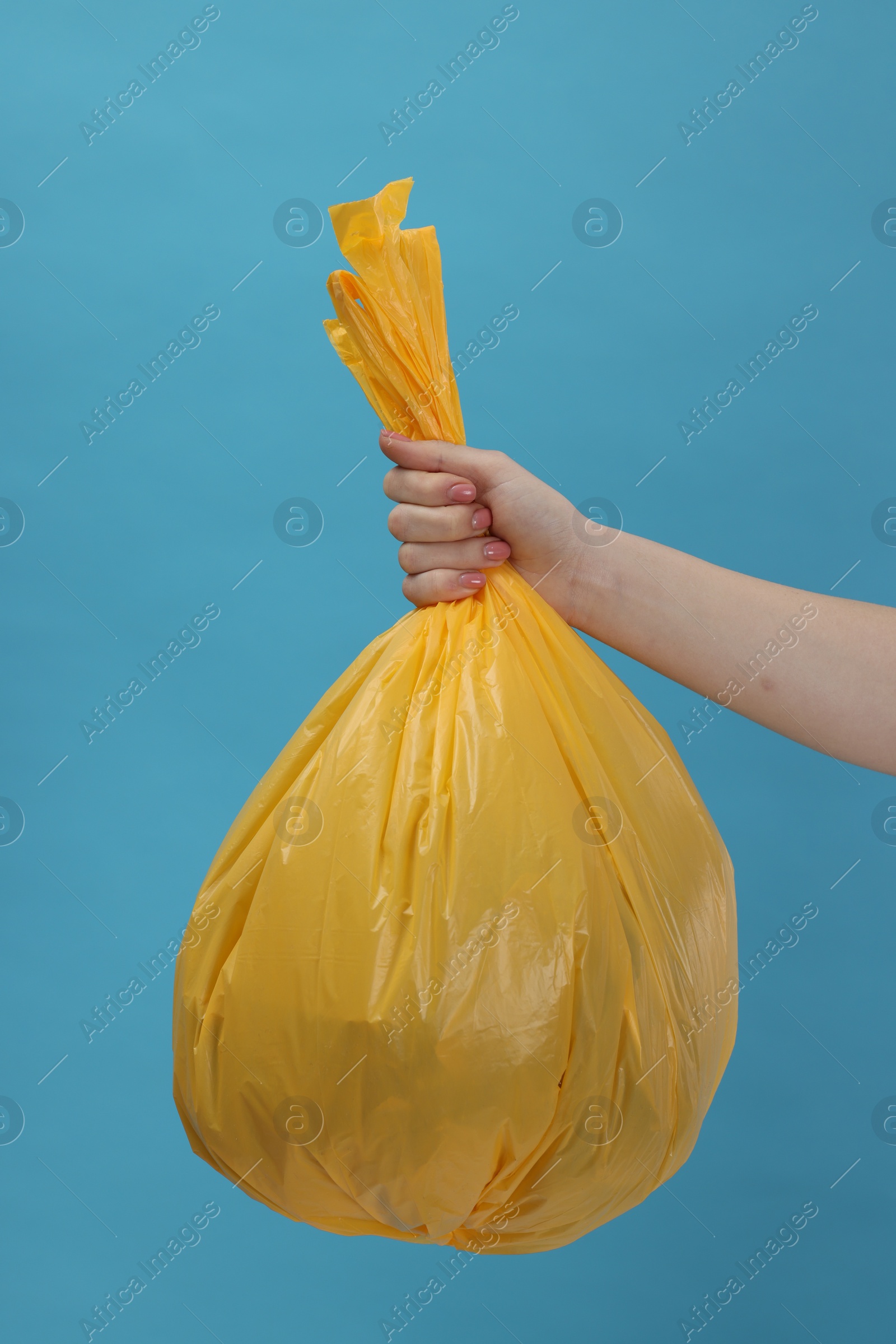 Photo of Woman holding plastic bag full of garbage on light blue background, closeup