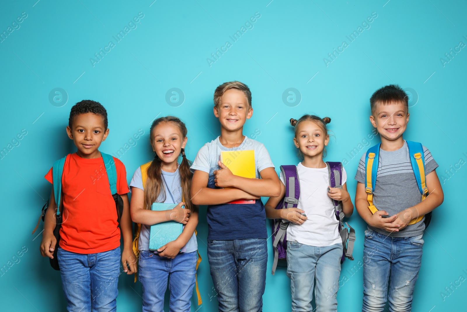 Photo of Group of little children with backpacks and school supplies on color background