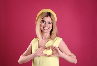 Portrait of woman making heart with her hands on color background