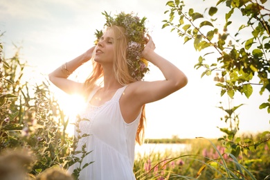 Photo of Young woman wearing wreath made of beautiful flowers outdoors on sunny day