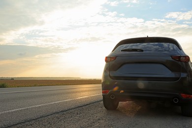 Photo of Black modern car parked on roadside at sunset, space for text
