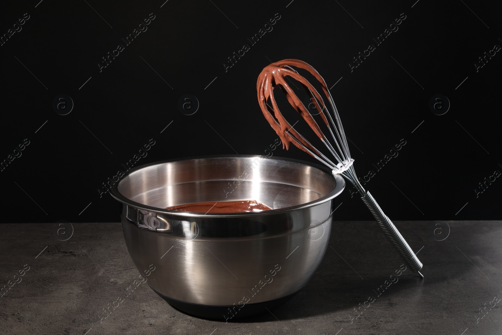 Photo of Bowl and whisk with chocolate cream on table against black background