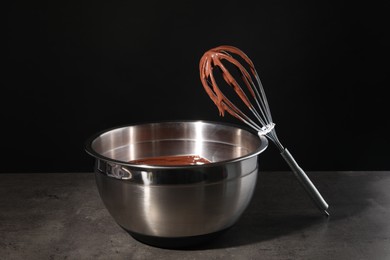 Bowl and whisk with chocolate cream on table against black background