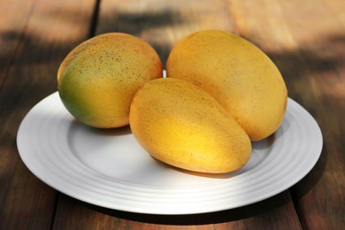 Plate with tasty mangoes on wooden table outdoors, closeup