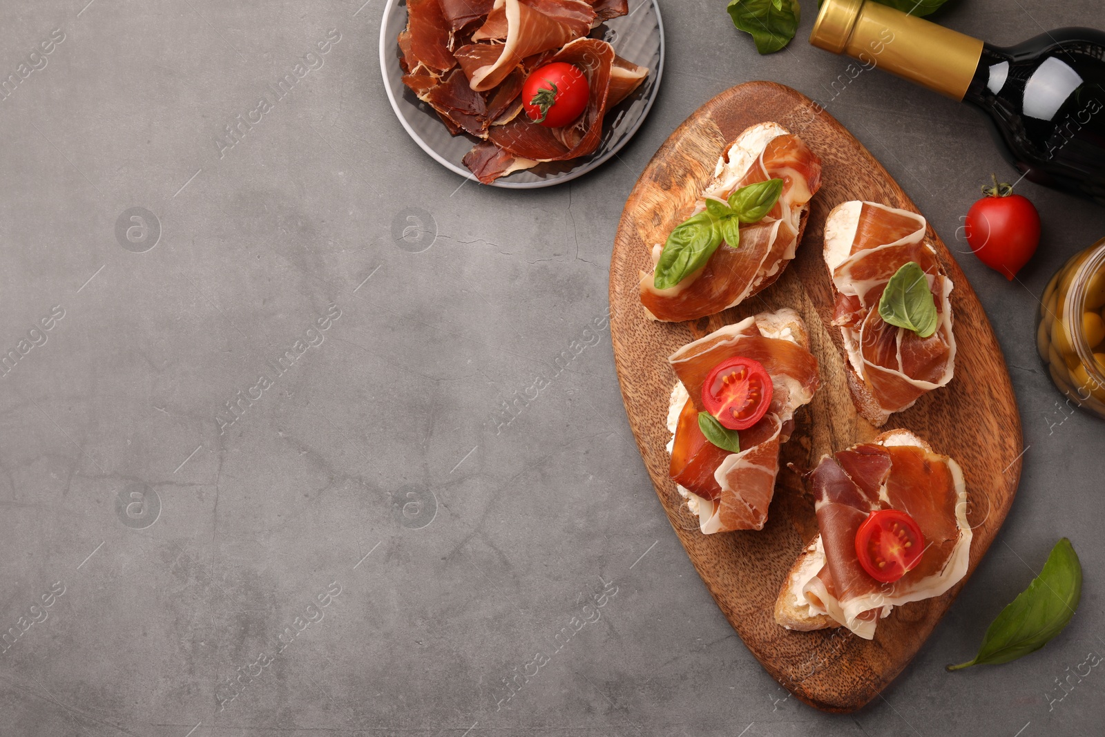 Photo of Tasty sandwiches with cured ham, basil and tomatoes on grey textured table, flat lay. Space for text