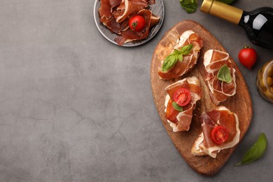 Tasty sandwiches with cured ham, basil and tomatoes on grey textured table, flat lay. Space for text