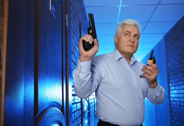 Photo of Professional security guard with gun and portable radio set in dark hallway