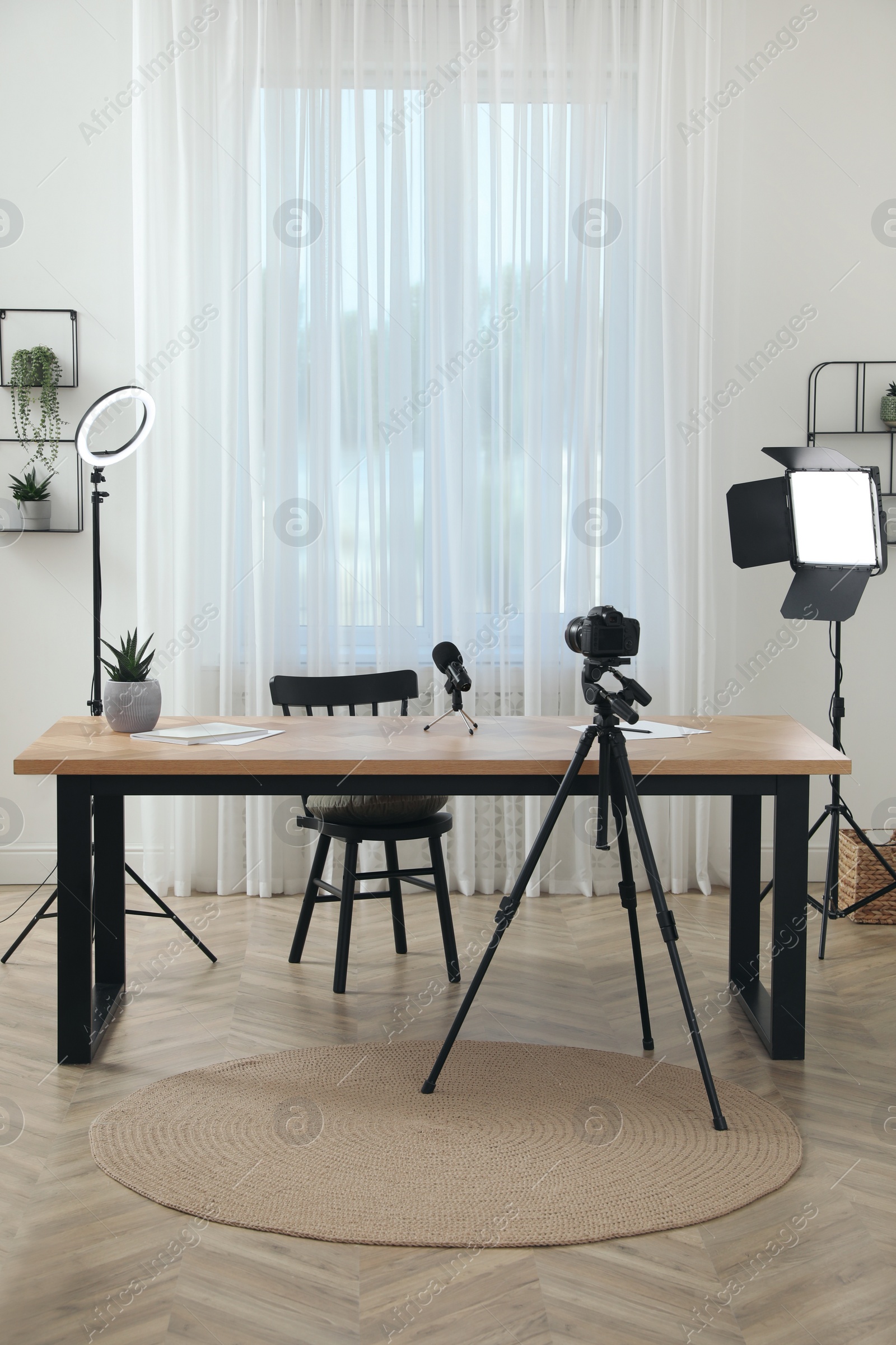 Photo of Camera and lighting equipment on tripods near table in room. Blogger workplace