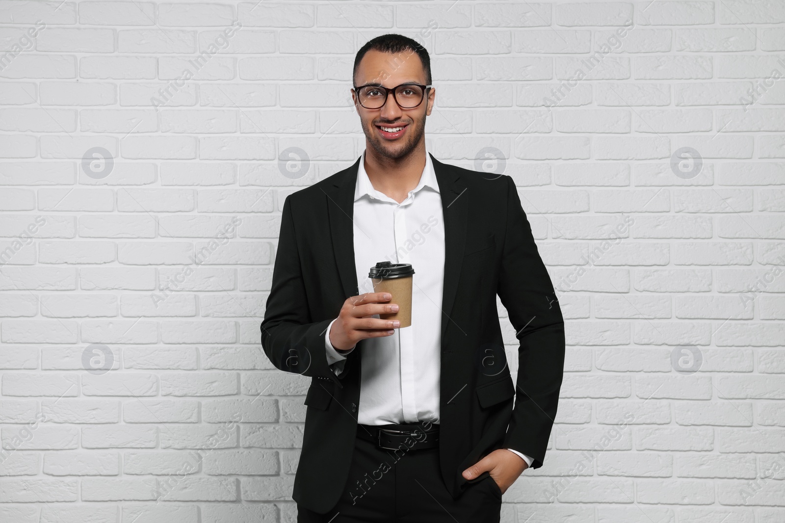 Photo of Young businessman in formal outfit with cup of drink near white brick wall