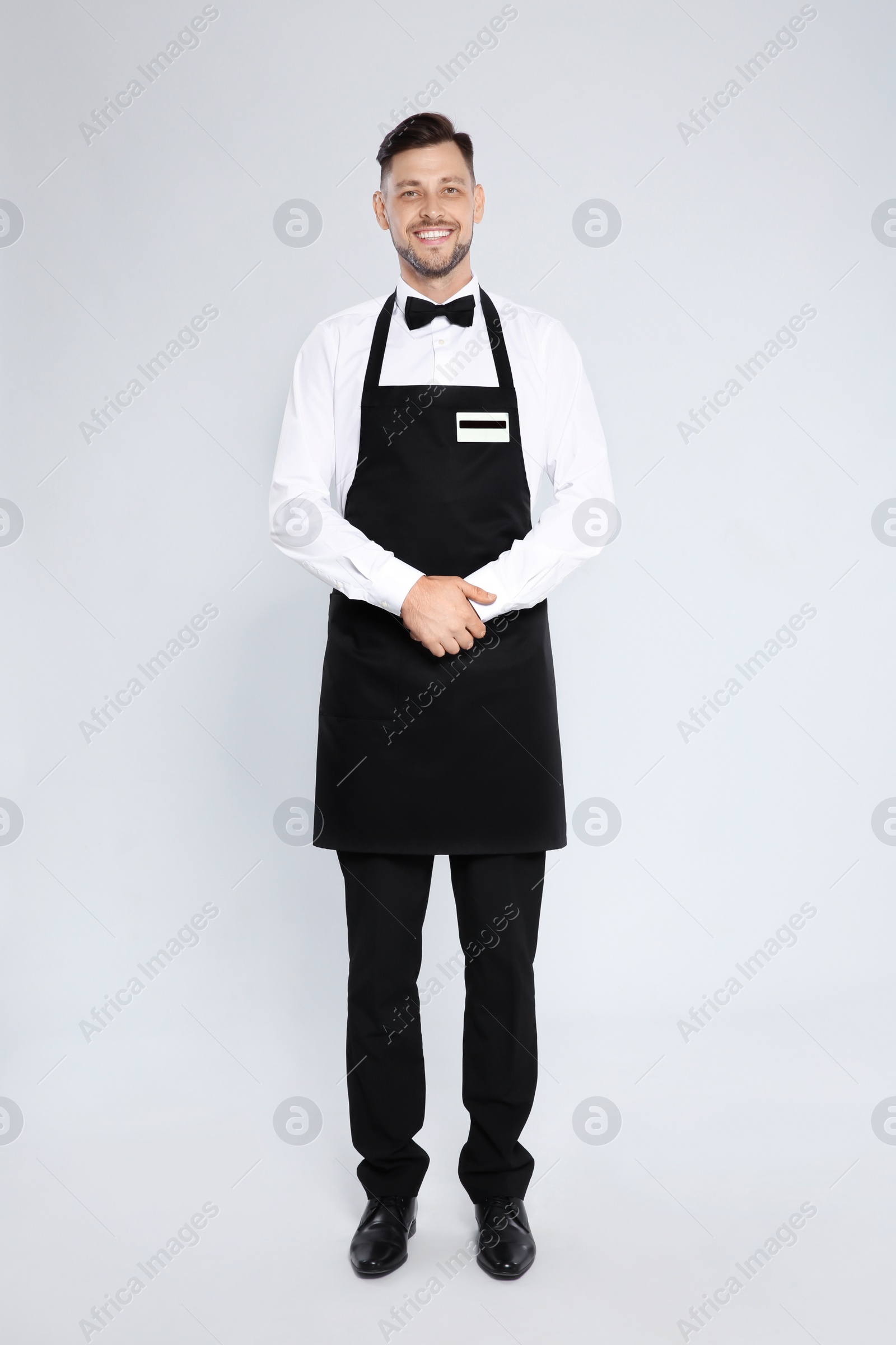 Photo of Full length portrait of handsome waiter in elegant uniform on light background