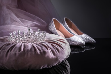 Photo of Pink pillow with beautiful silver tiara near shoes on black table