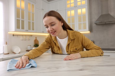 Woman with microfiber cloth cleaning white marble table in kitchen