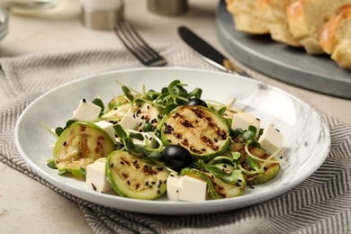 Photo of Delicious salad with grilled zucchini slices, feta cheese and olives on light grey table, closeup