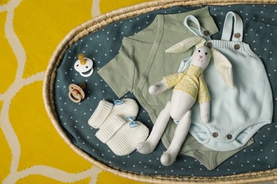 Basket with baby clothes and accessories on yellow fabric, top view